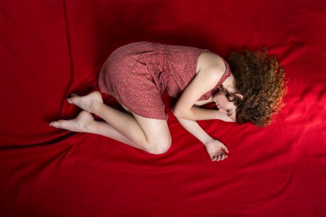 Beautiful sad woman is lying on red blanket